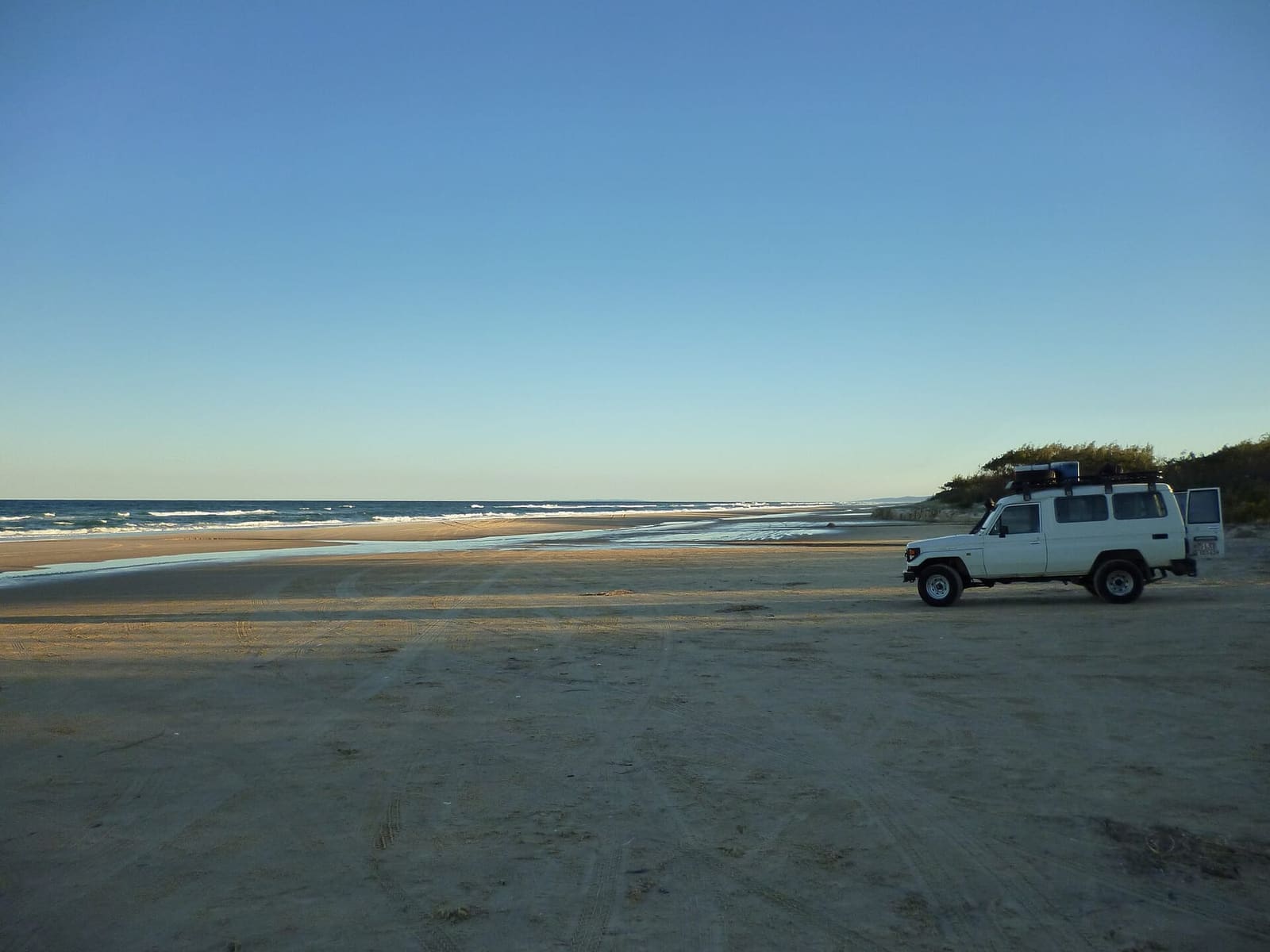 A white 4WD parked on a K'gari beach at dusk