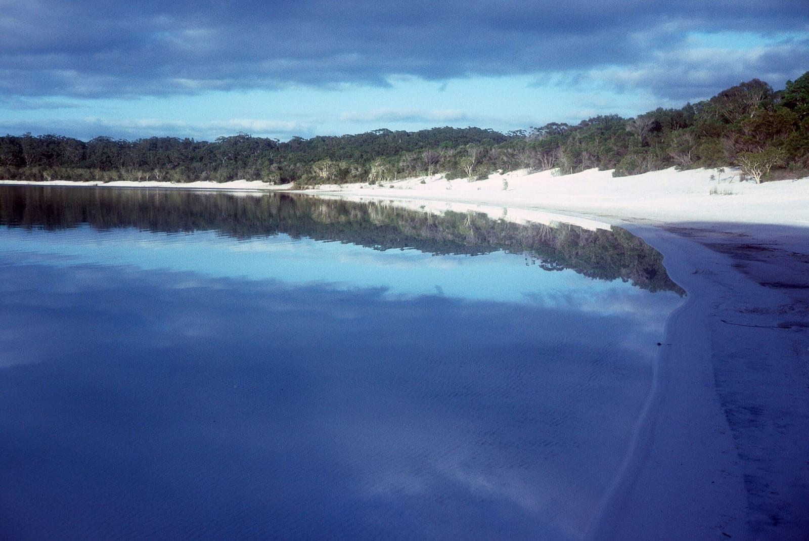 Lake McKenzie's white-sand shore and deep blue water reflecting clouds