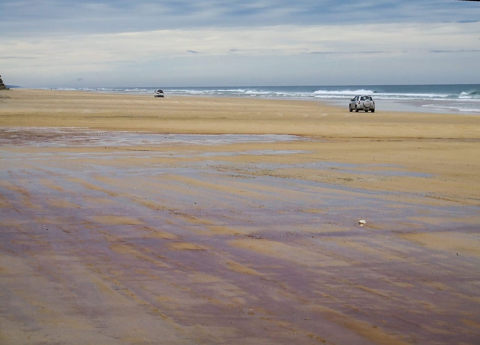 Wide, flat 75 Mile Beach on K'gari with a 4WD in the distance